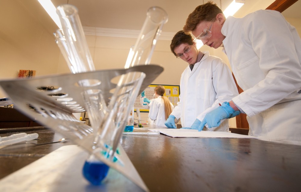 Dos alumnos con bata y guantes trabajan en un laboratorio